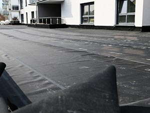 EPDM-Roofing-McKinney-TX-Texas-1 | Anderson Industrial Roofing Flat rooftop surface covered with black waterproof membrane, with a modern white building and windows in the background.