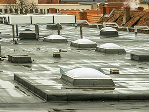 EPDM-Roofing-McKinney-TX-Texas-2 | Anderson Industrial Roofing Aerial view of a flat commercial roof dotted with white dome skylights and vents, with brick buildings in the background.