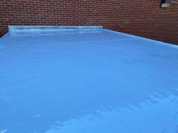 Flat roof covered with bright blue waterproof membrane against a red brick wall on the background field edge