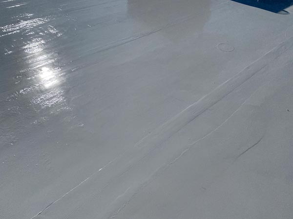 Close-up of a smooth light-gray surface with faint seam lines and sun glare, with a hint of blue at the top edge.