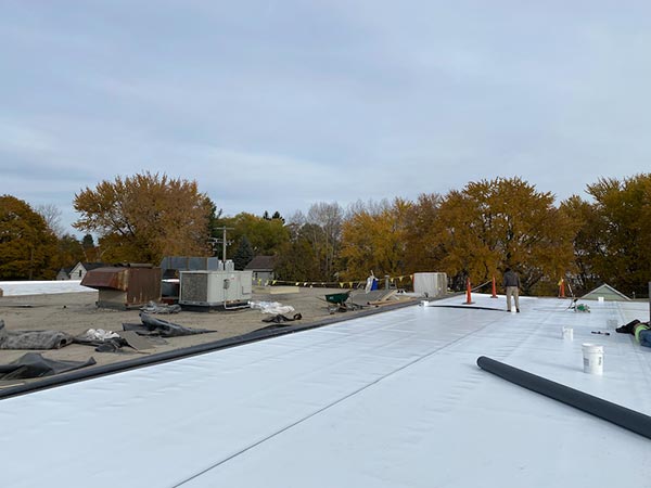 Single-Ply-Roofers-McKinney-TX-Texas-1 | Anderson Industrial Roofing Rooftop under construction with white membrane, HVAC units, and a worker with autumn trees in the background.