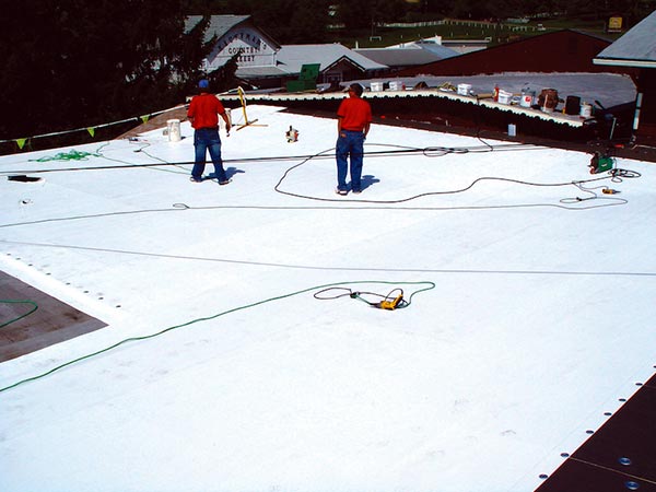 Single-Ply-Roofers-McKinney-TX-Texas-2 | Anderson Industrial Roofing Two workers in red shirts stand on a white flat roof with hoses and tools scattered around.